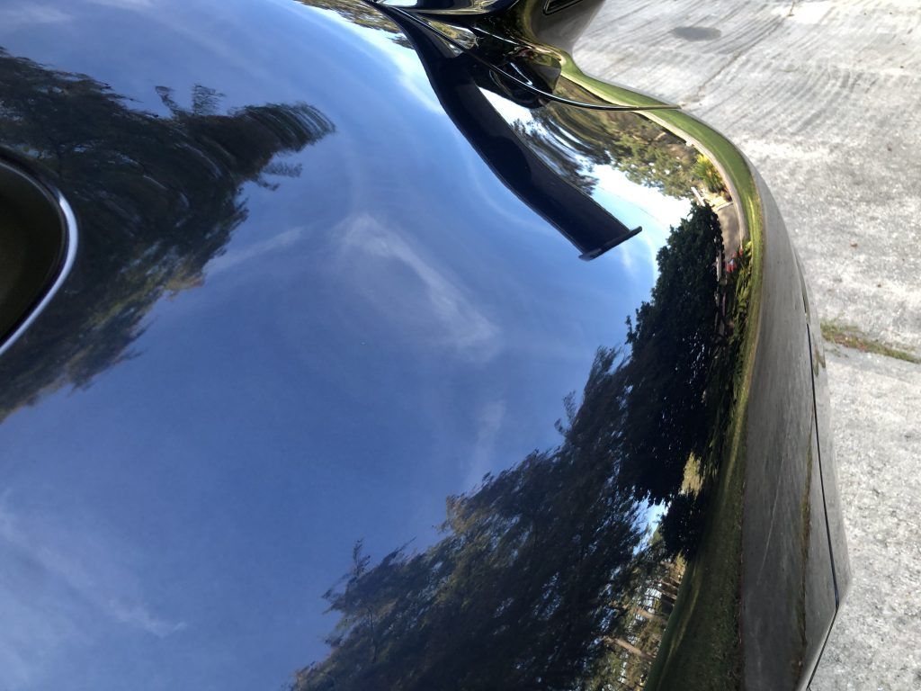 A close up of a black car with trees reflected in it