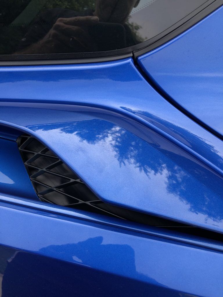 A close up of a blue car with a reflection of trees