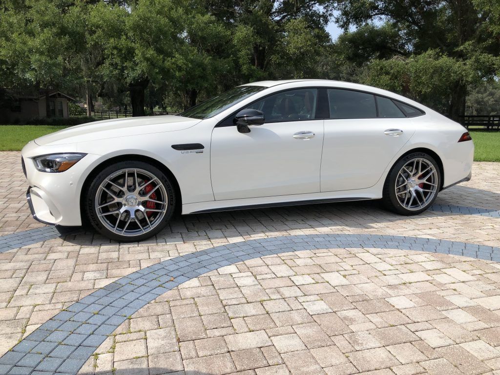 A white mercedes amg gt 63 s is parked on a brick driveway.