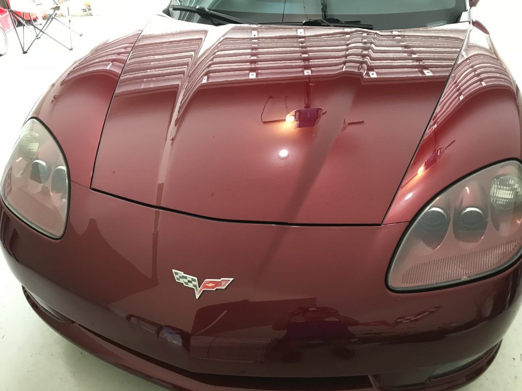 A red sports car with the hood up is parked in a garage