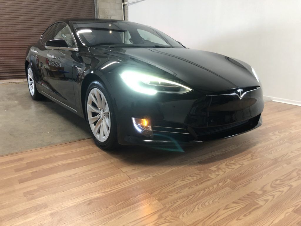 A black tesla model s is parked on a wooden floor in a garage.