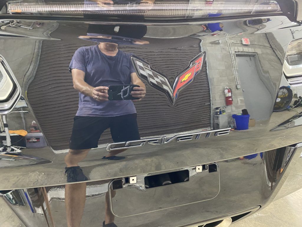 A man is taking a picture of himself in the mirror of a corvette.