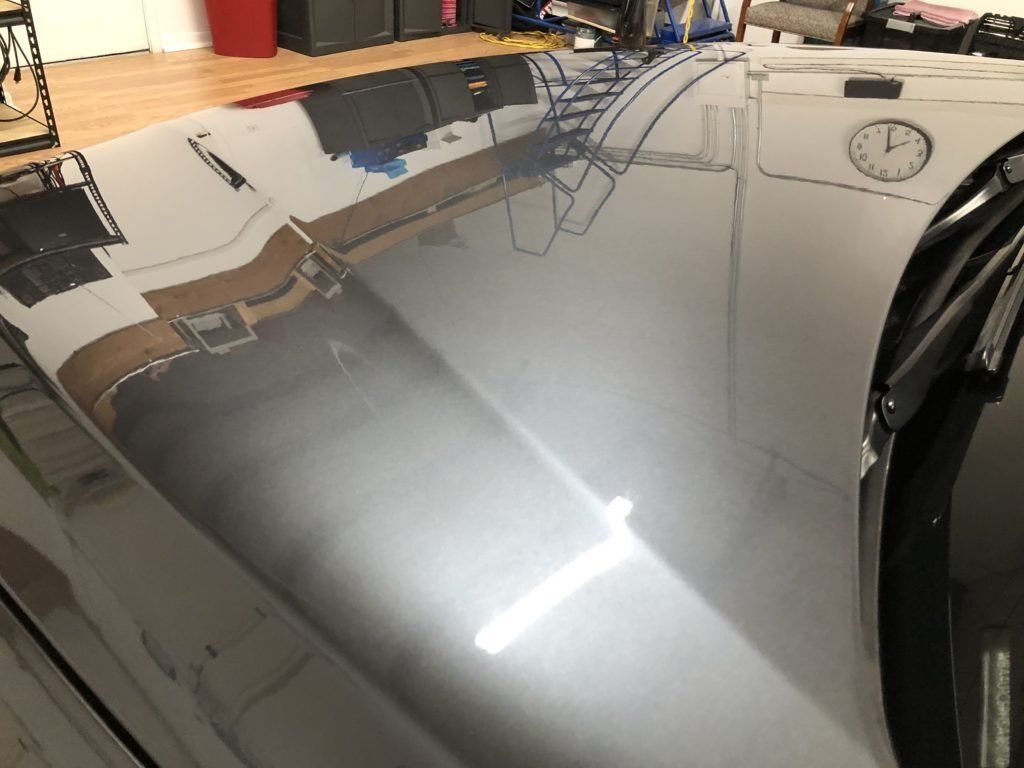 A black car is parked in a garage with a clock on the wall.