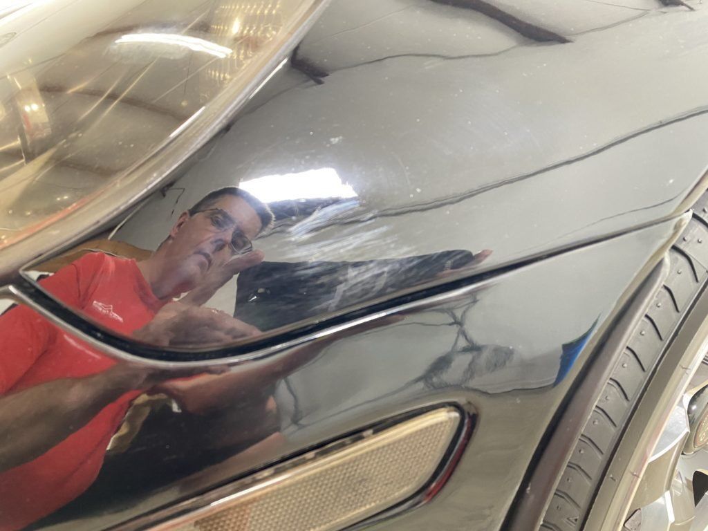 A man in a red shirt is reflected in the headlight of a car.