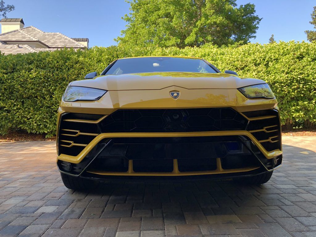 A yellow lamborghini urus is parked in a driveway.
