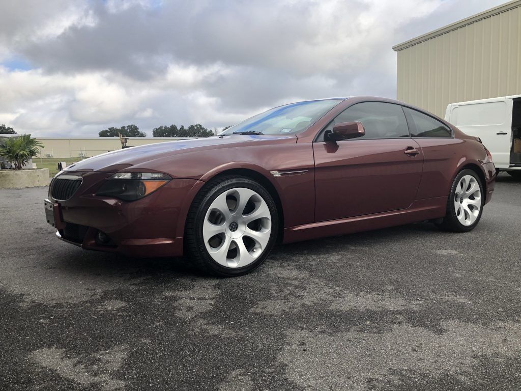 A maroon bmw 6 series coupe is parked in a parking lot in front of a building.