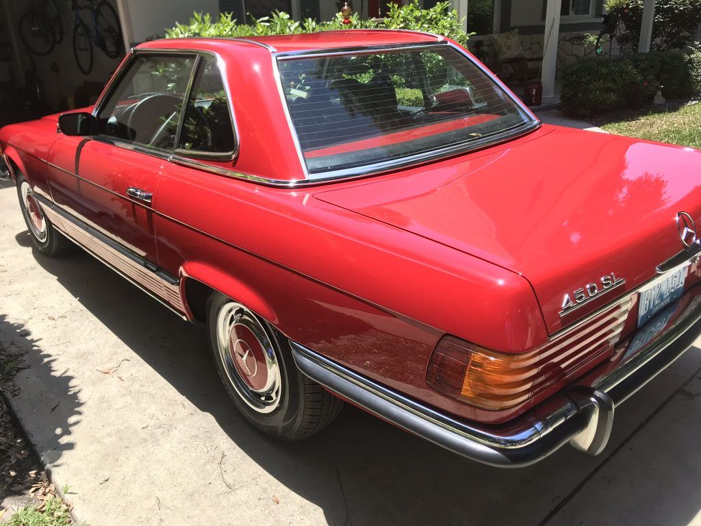 A red car is parked in a driveway in front of a house.