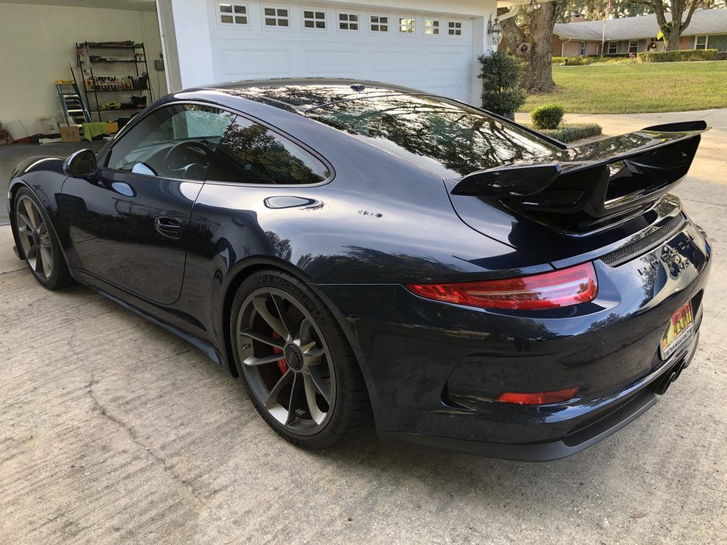 A black porsche 911 gt3 is parked in front of a garage.