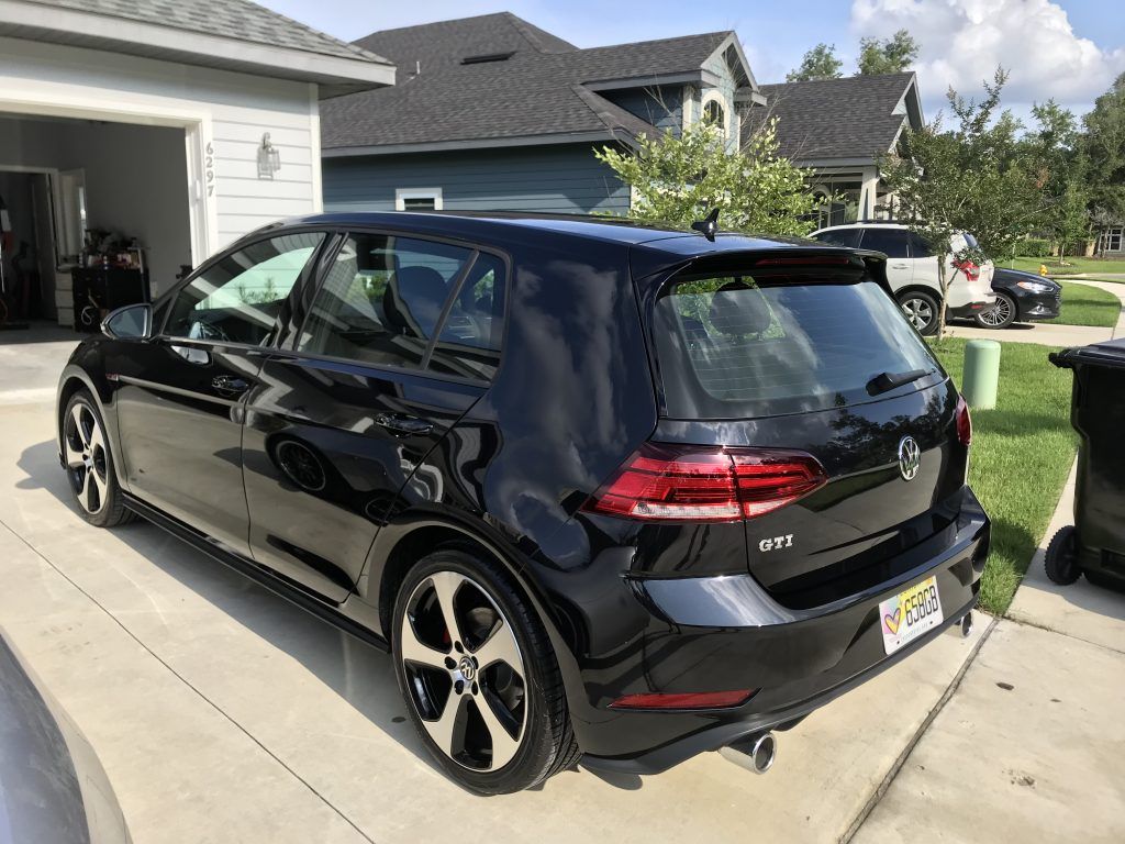 A black volkswagen golf is parked in a driveway in front of a house.