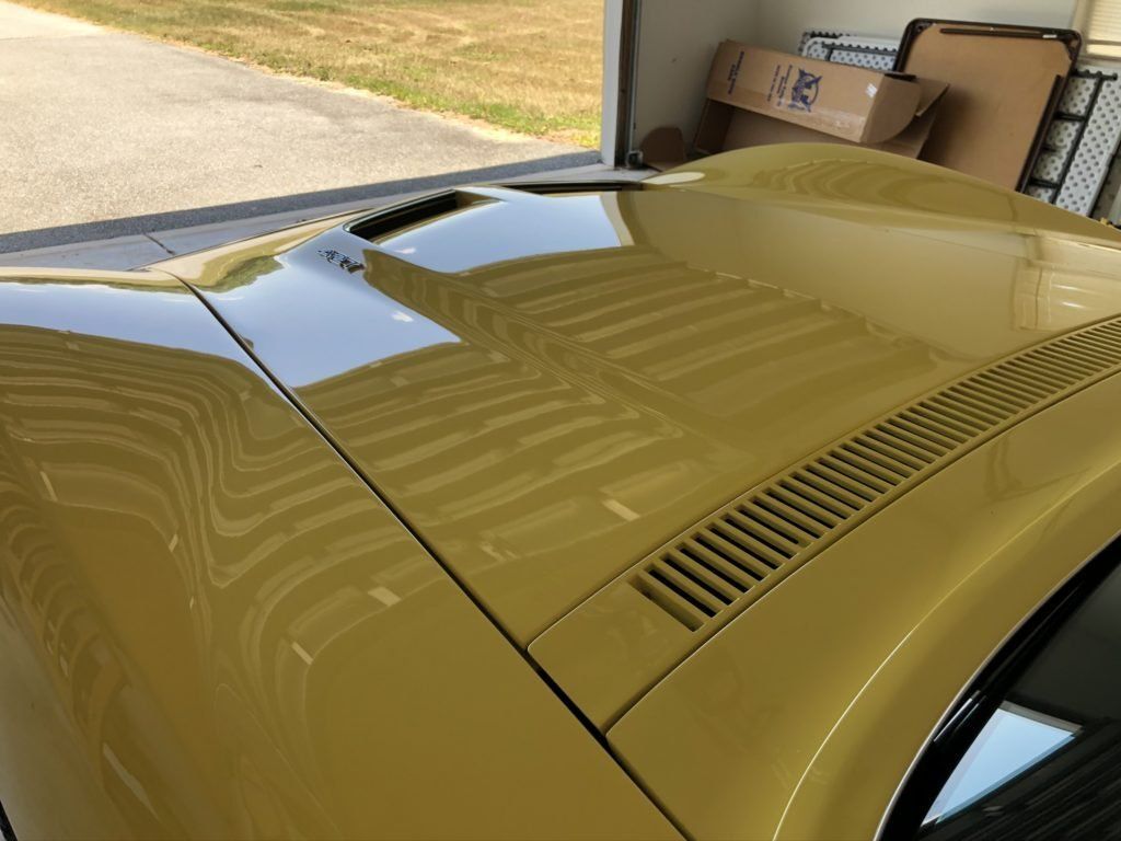 The hood of a yellow car is sitting in a garage.