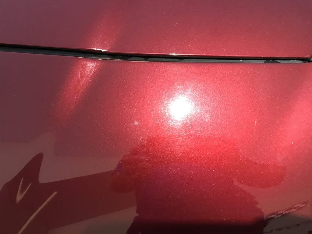A close up of a red car hood with a reflection of a person taking a picture.