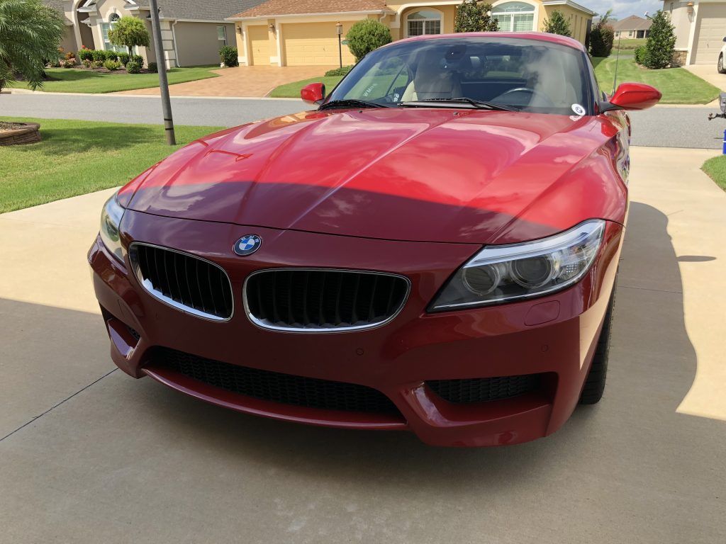 A red bmw z4 is parked in a driveway in front of a house.