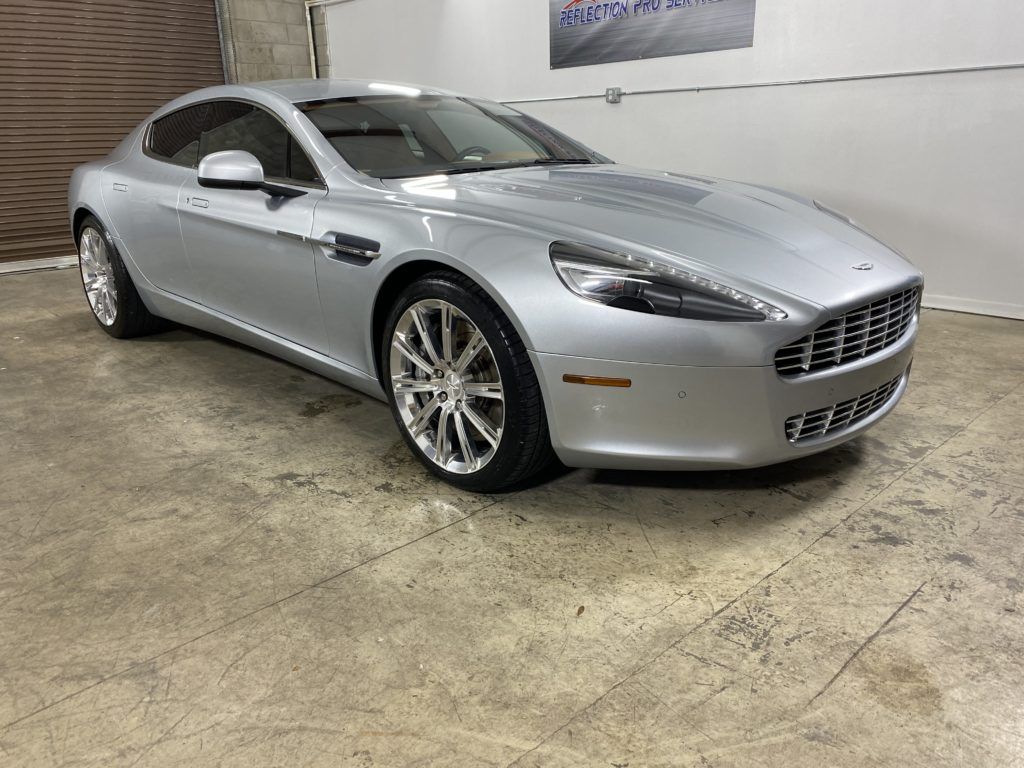 A silver aston martin rapide is parked in a garage.