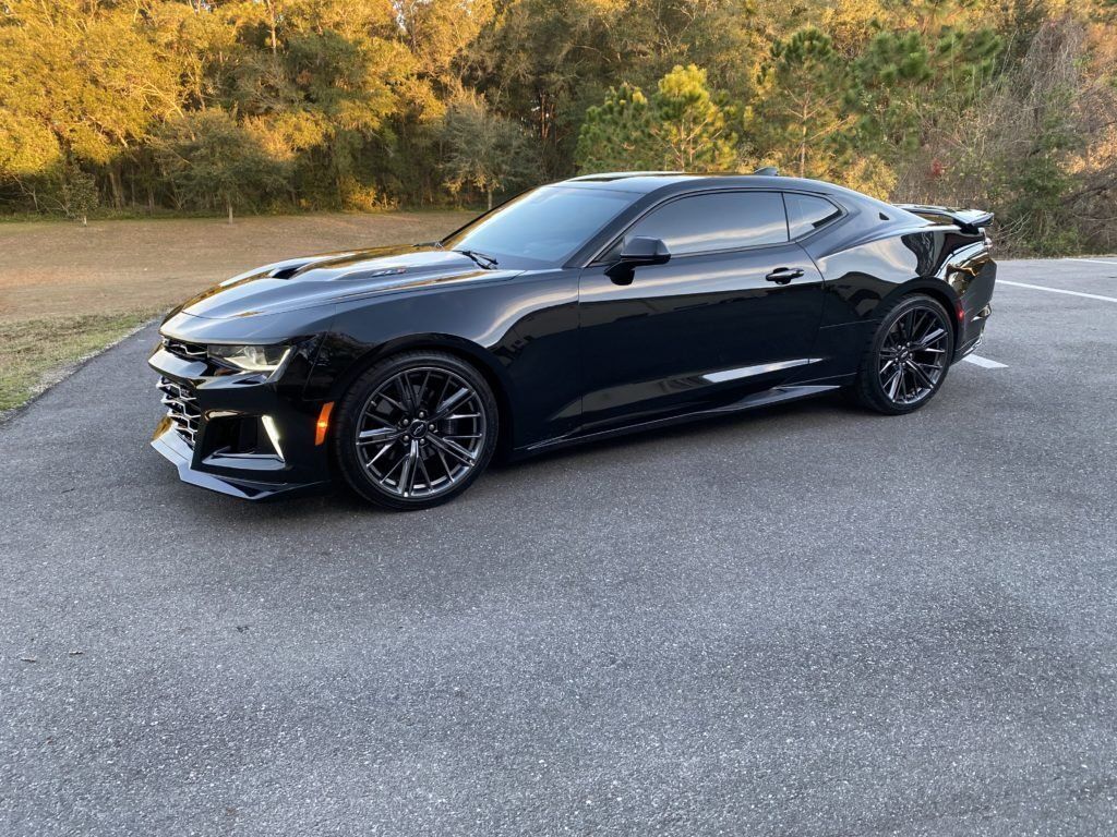 A black chevrolet camaro is parked on the side of the road.