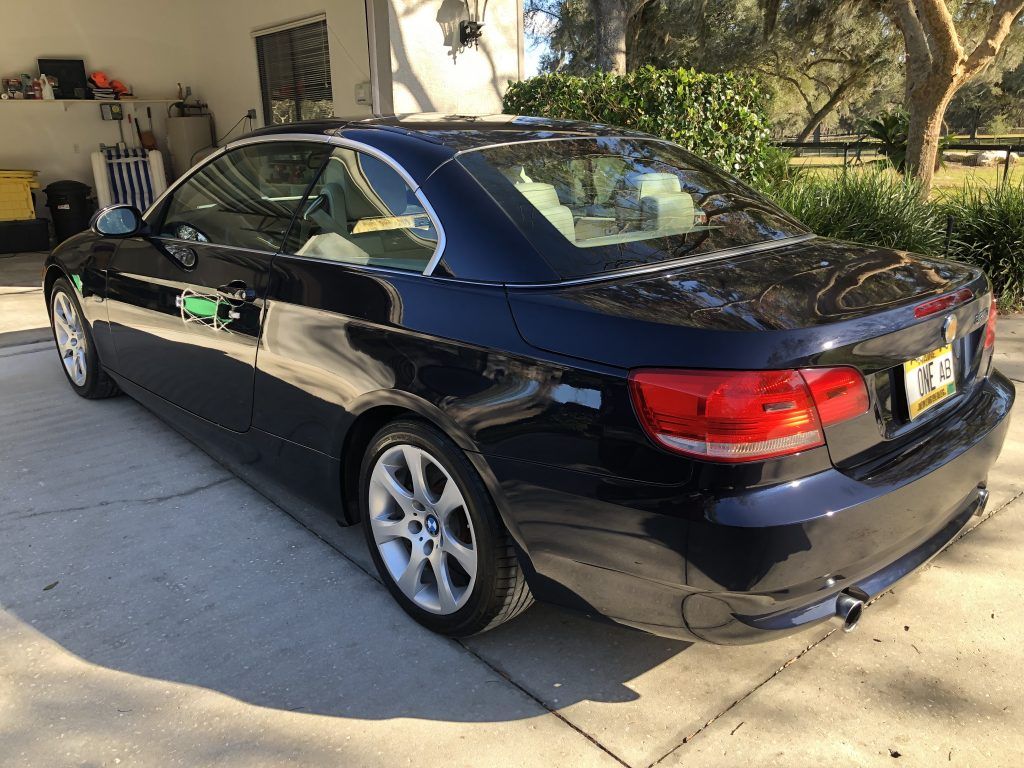 A black bmw 3 series convertible is parked in a driveway.