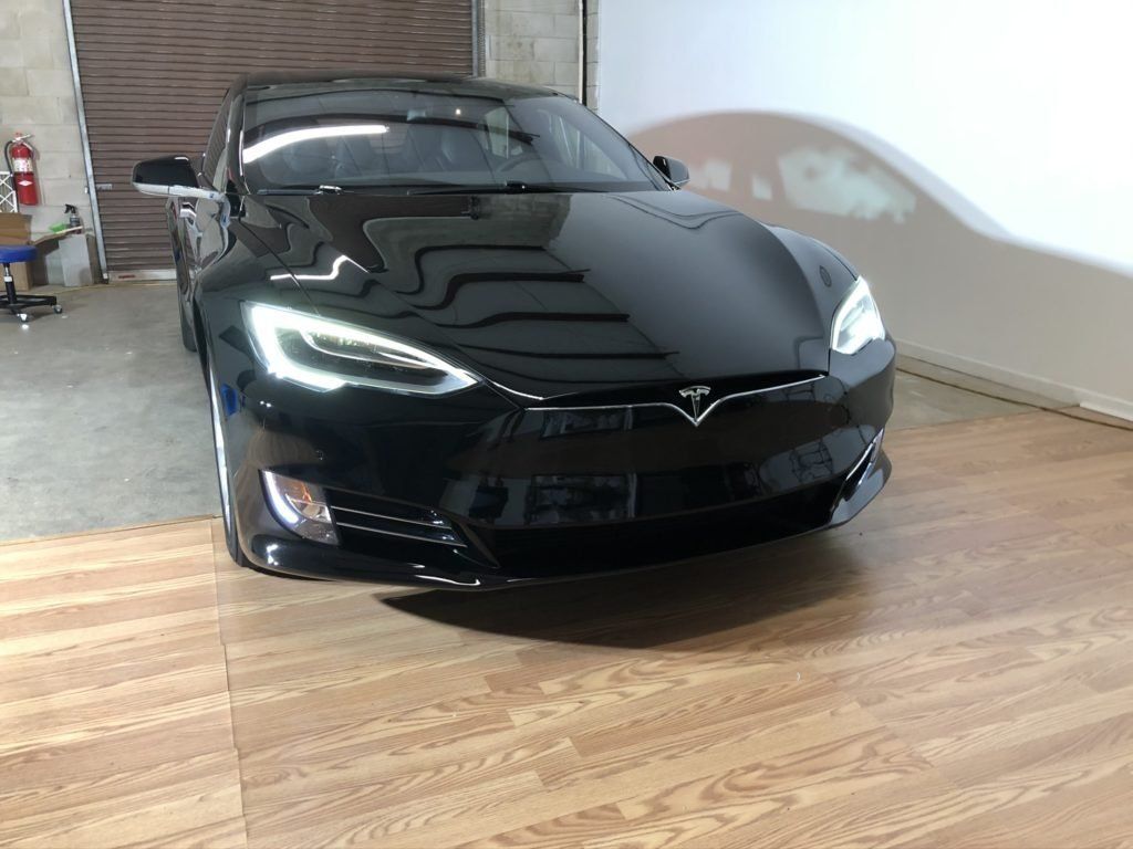 A black tesla model s is parked on a wooden floor in a garage.