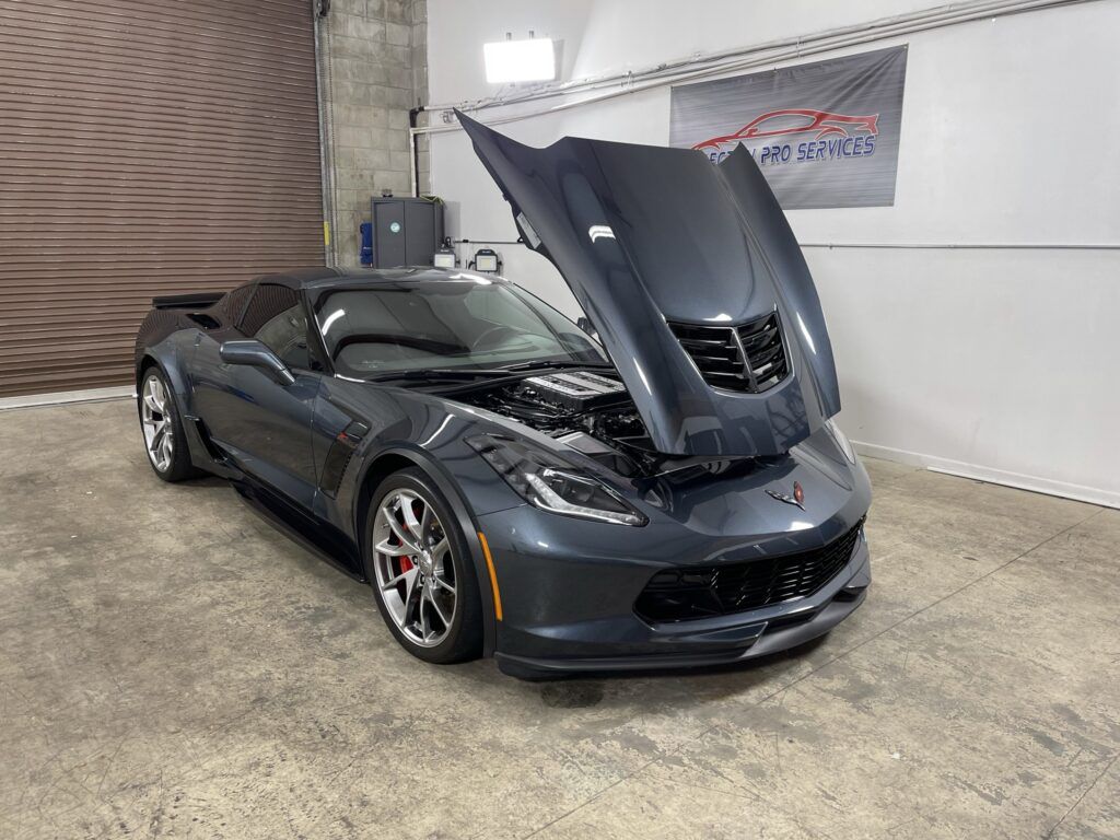 A gray corvette with its hood up is parked in a garage.