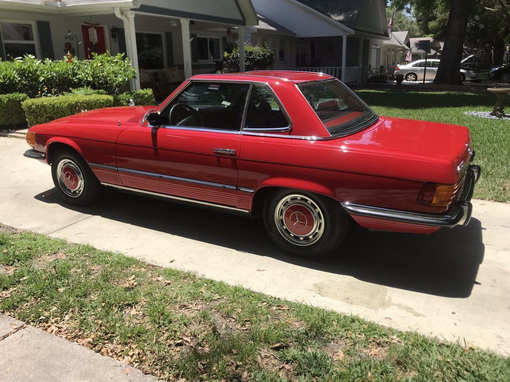 A red car is parked on the side of the road in front of a house.