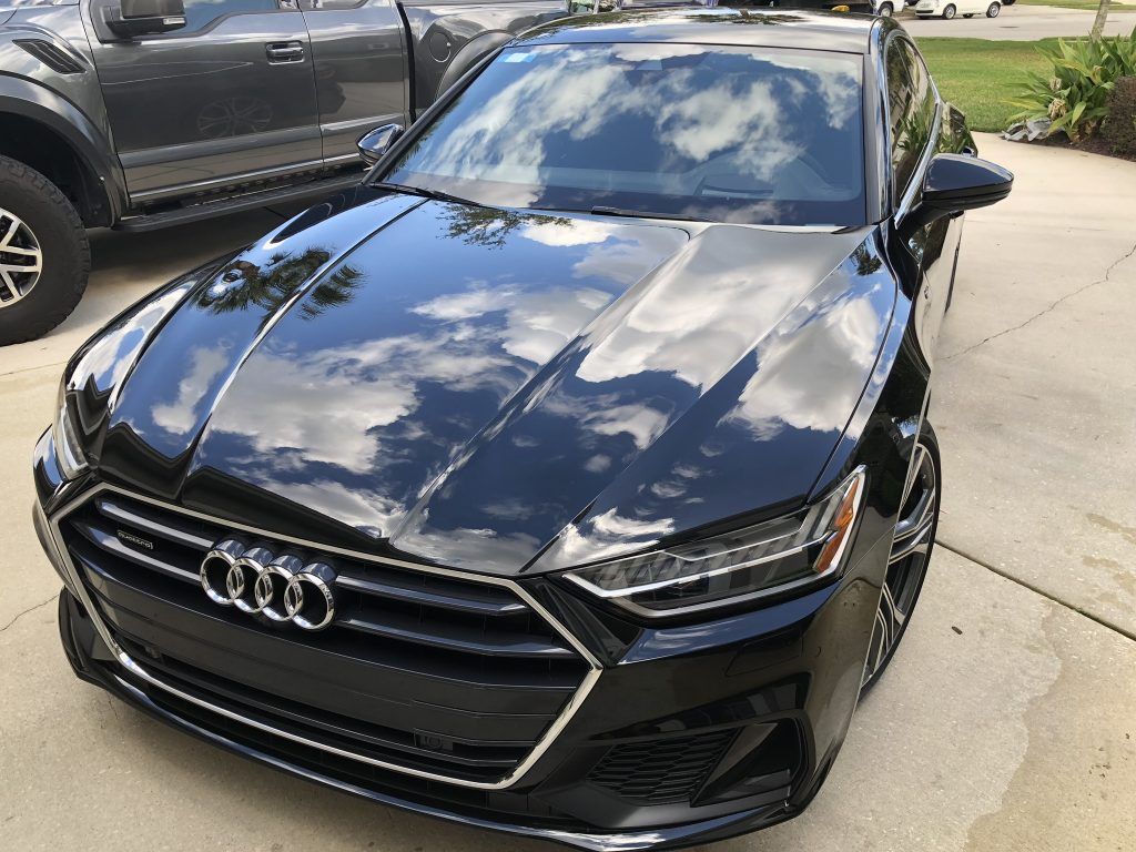A black audi a7 is parked in a driveway next to a truck.