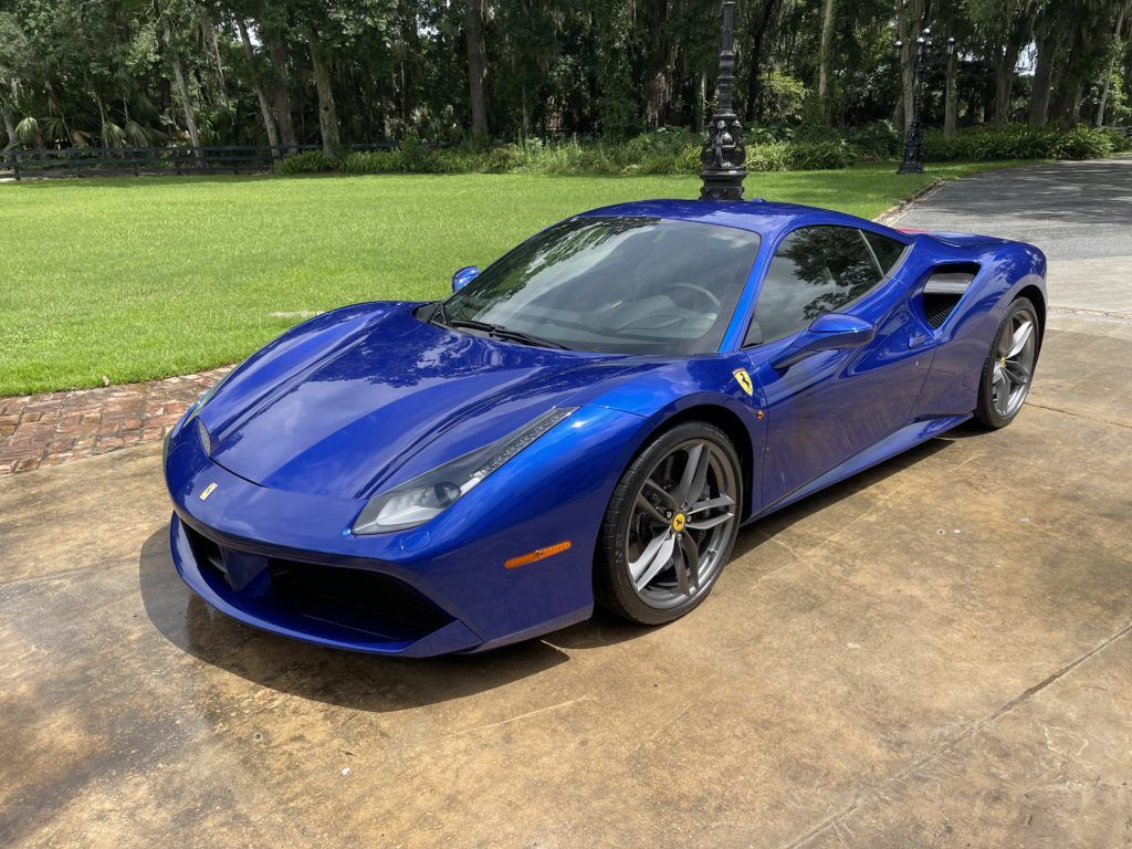A blue ferrari 488 gtb is parked in a driveway.