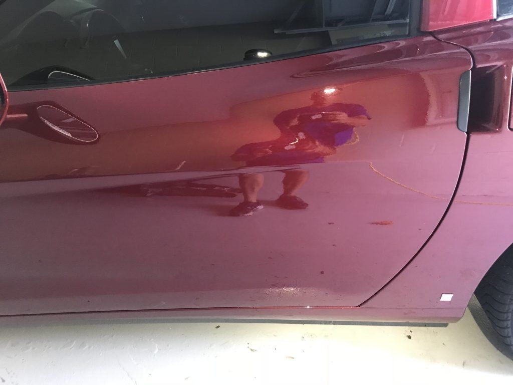 A man is reflected in the door of a red car