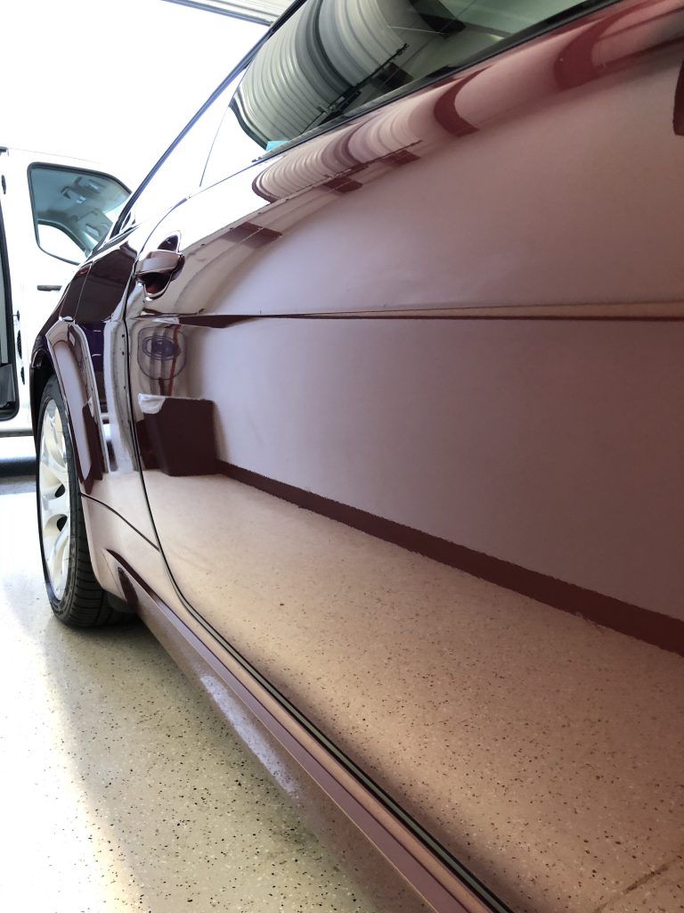 A red car is parked in a garage with a white van in the background.
