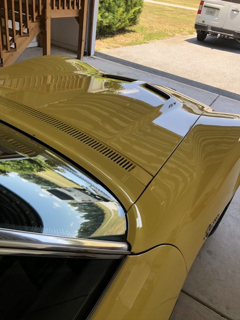 A yellow car is parked in a garage with the hood up.