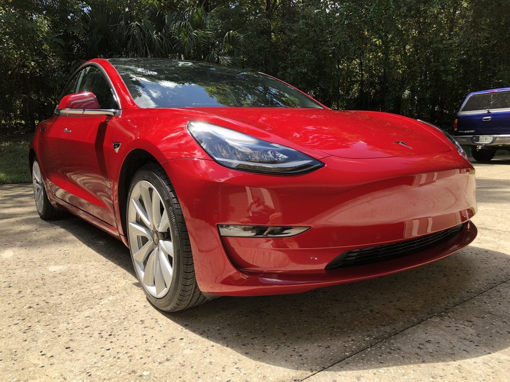A red tesla model 3 is parked in a driveway.