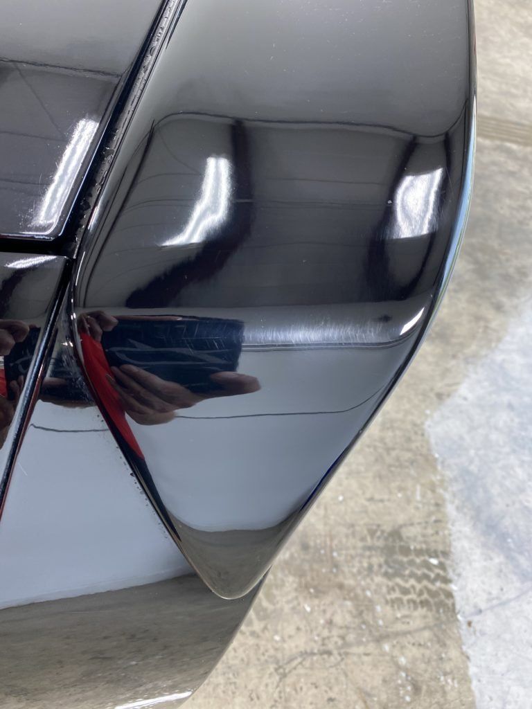 A close up of a black car with a reflection of a person in it.