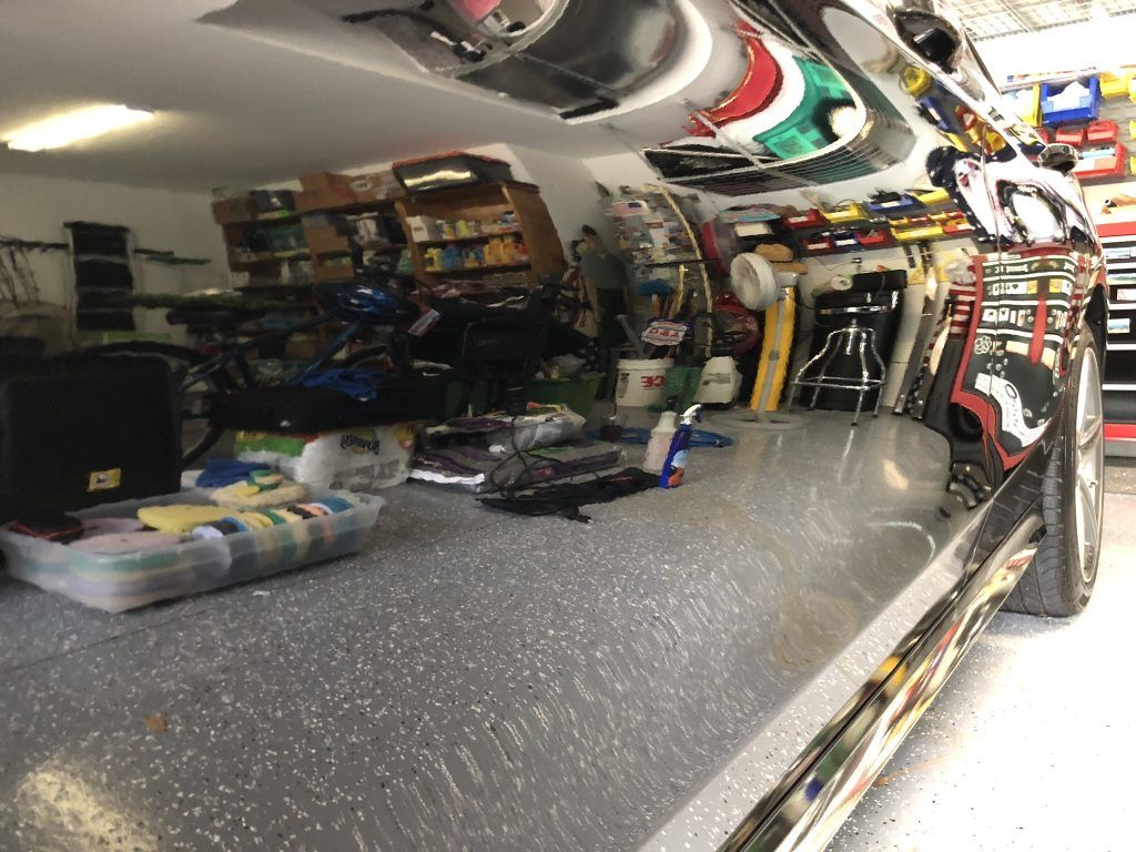 A car is parked in a garage with a lot of tools on the floor.