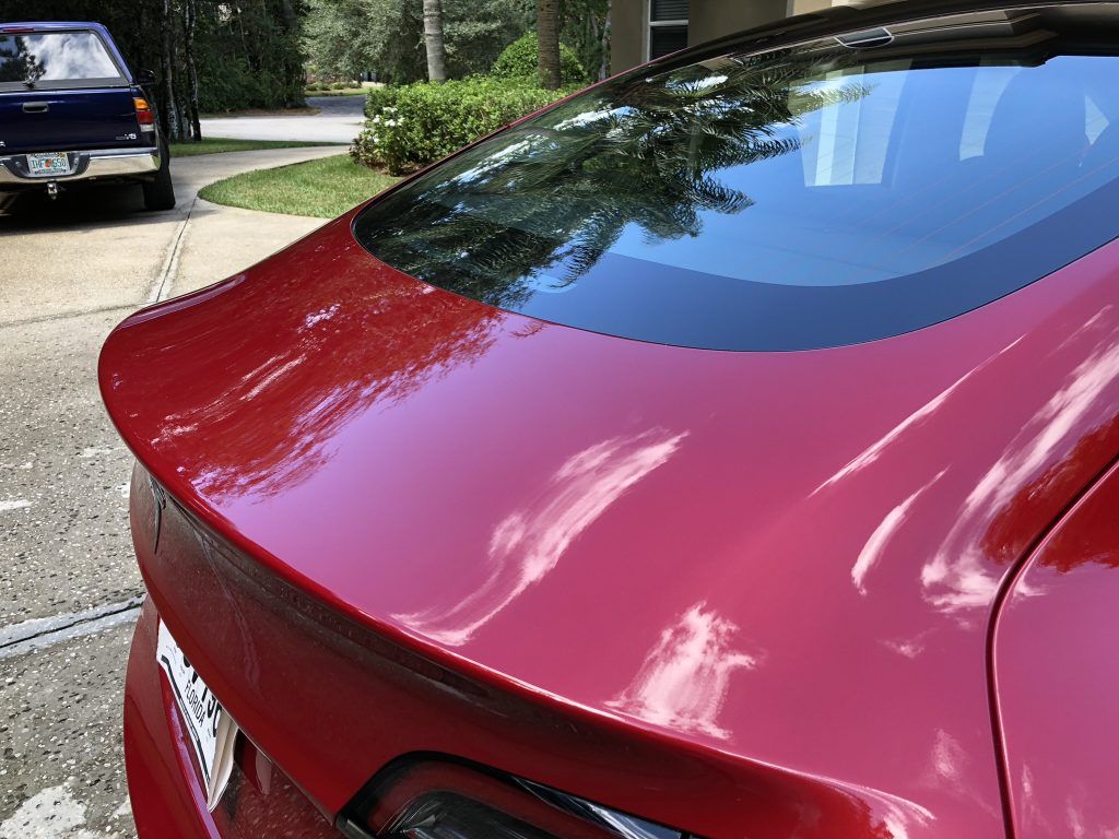 A red car is parked in a driveway next to a blue truck