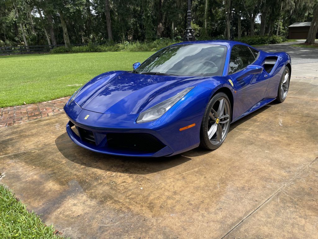 A blue ferrari 488 gtb is parked in a driveway.