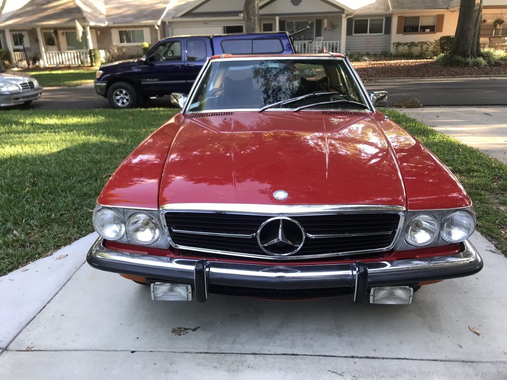 A red mercedes benz is parked in a driveway in front of a house.