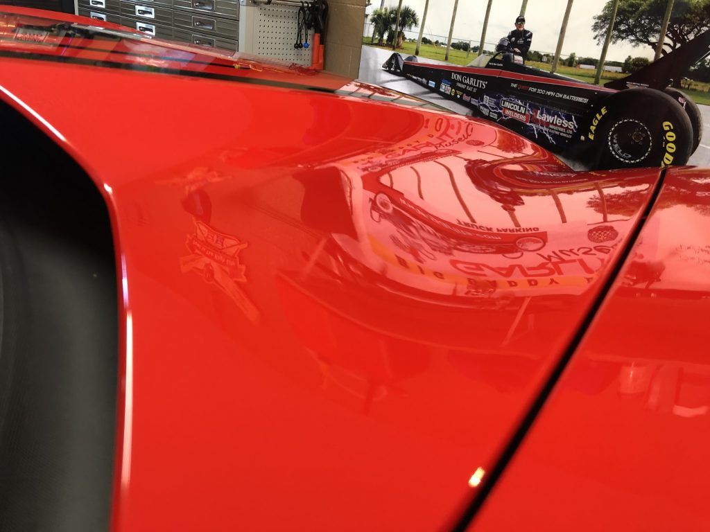 A close up of a red car with a race car in the background.