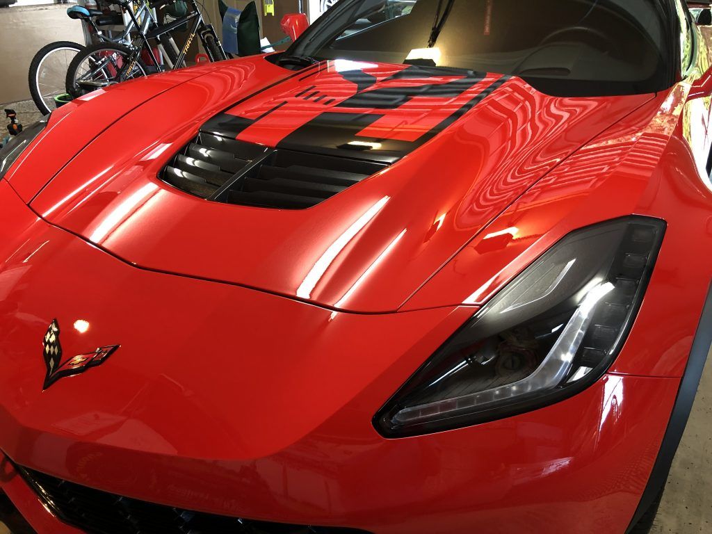 A red sports car with black stripes on the hood is parked in a garage.