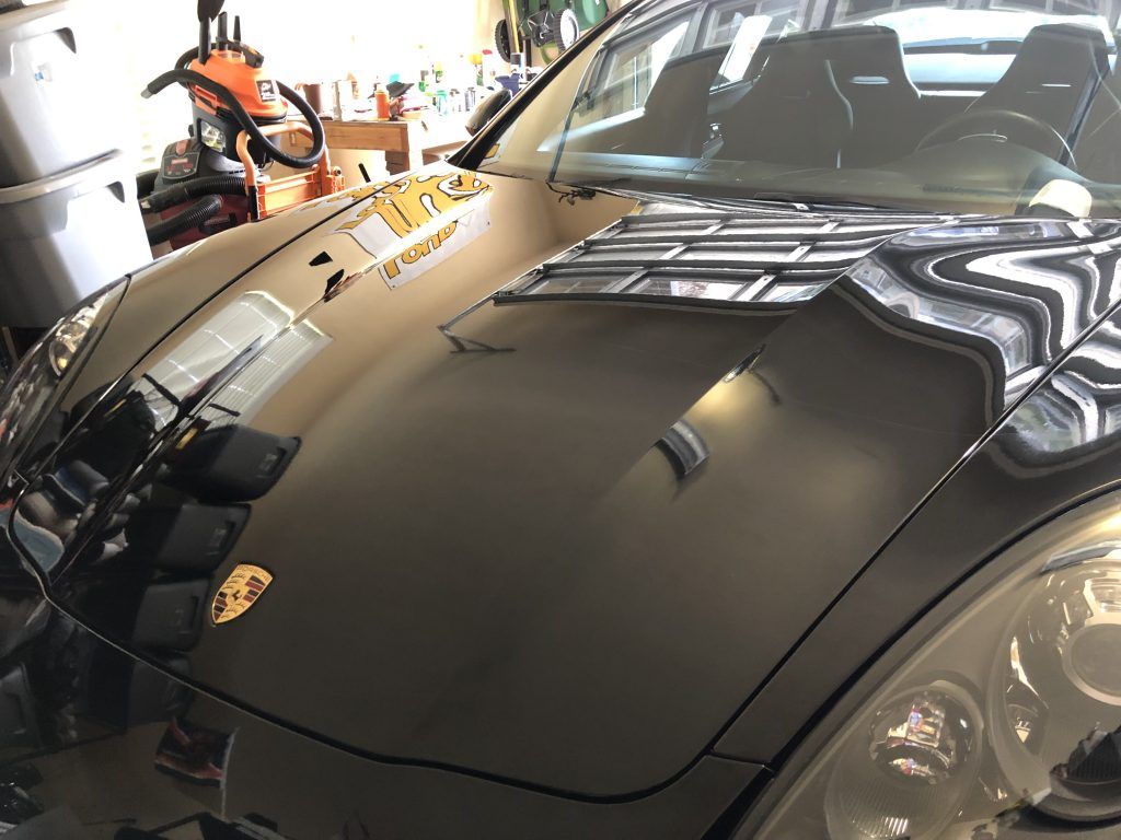 A black car is parked in a garage with the hood open.