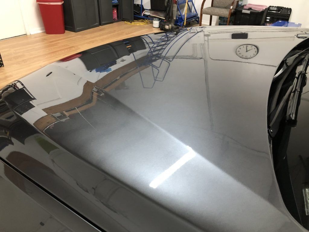 A black car is parked in a garage with a clock on the wall.