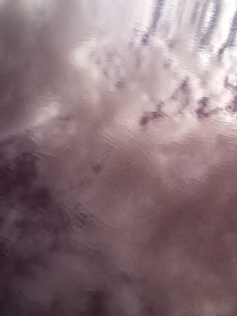 A close up of a purple background with clouds reflected in it.