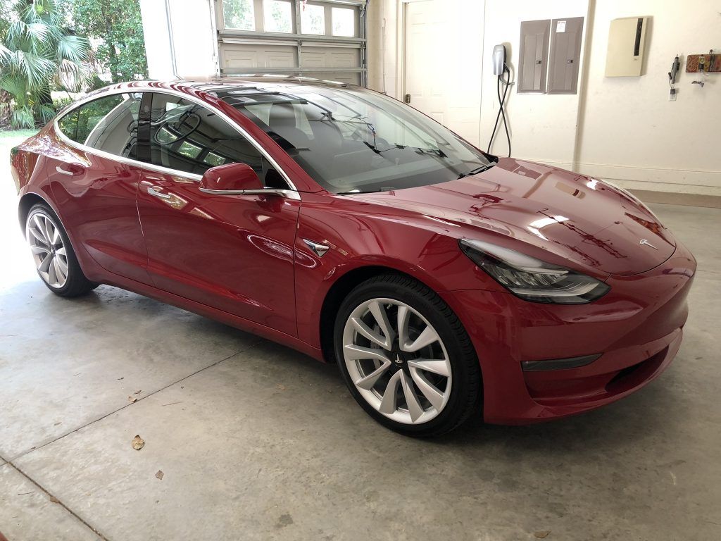 A red tesla model 3 is parked in a garage.