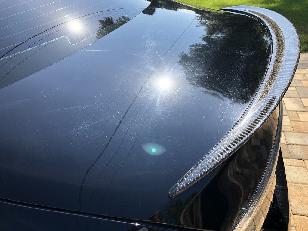 A black car with a spoiler on the back is parked on a brick driveway.
