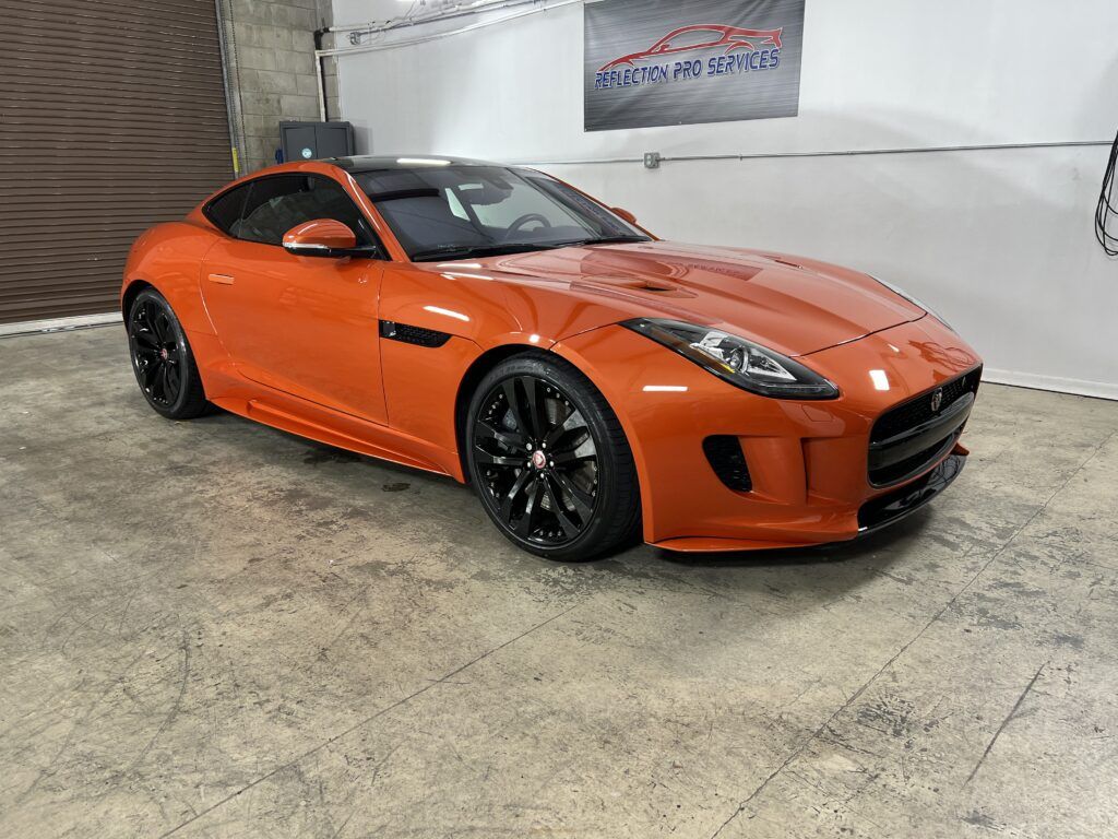 An orange jaguar f type is parked in a garage.