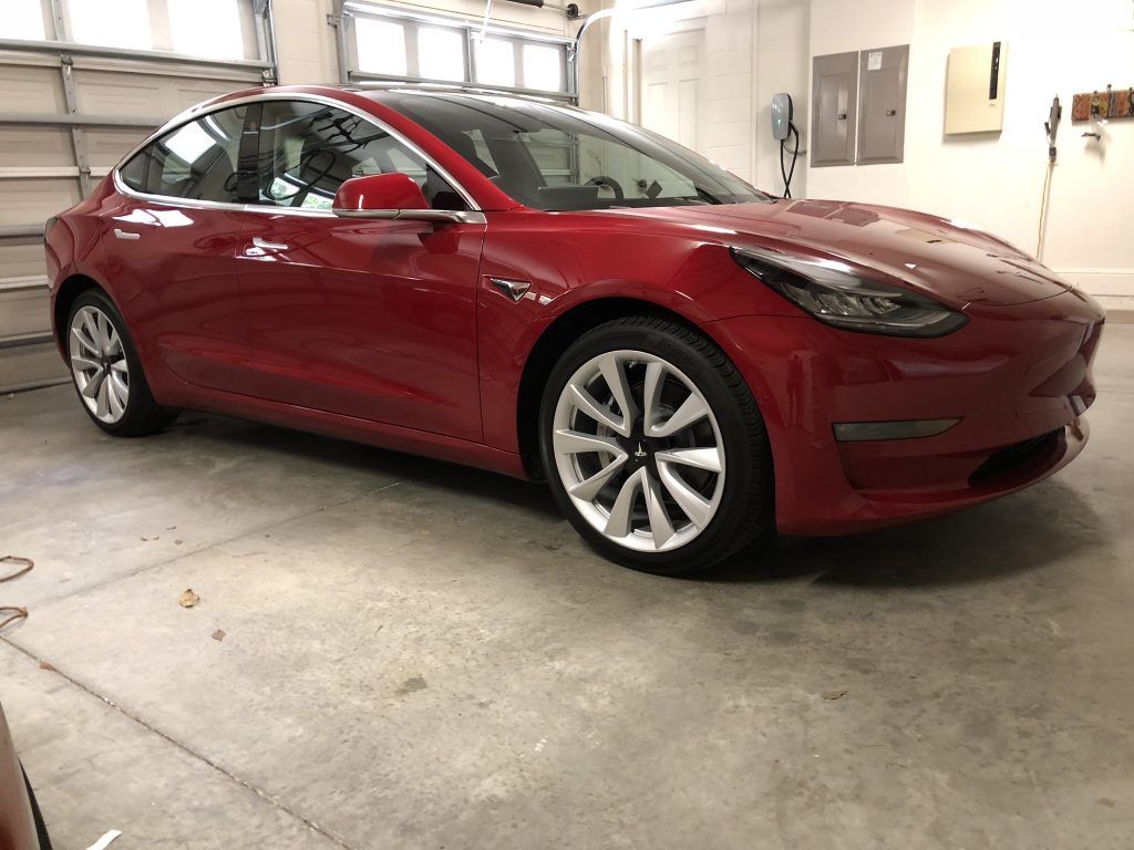 A red tesla model 3 is parked in a garage.