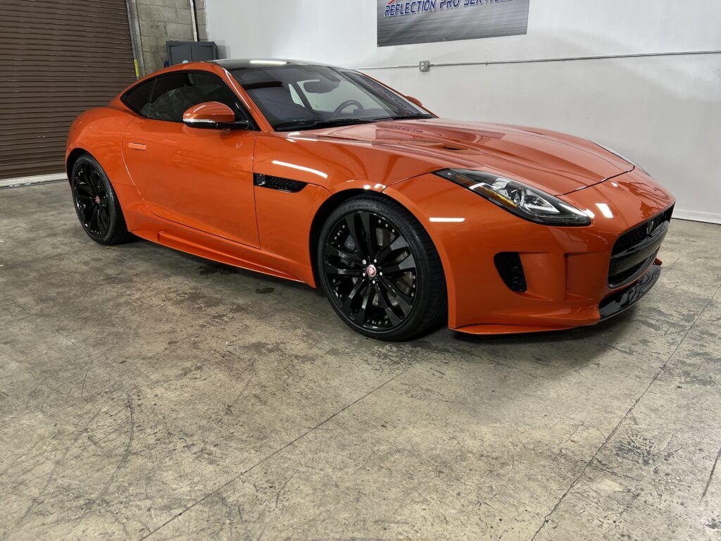 An orange jaguar f type is parked in a garage.