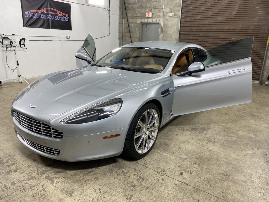 A silver sports car is parked in a garage with its doors open.