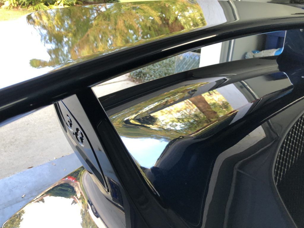A black car is parked in a garage with a reflection of trees in the windshield.