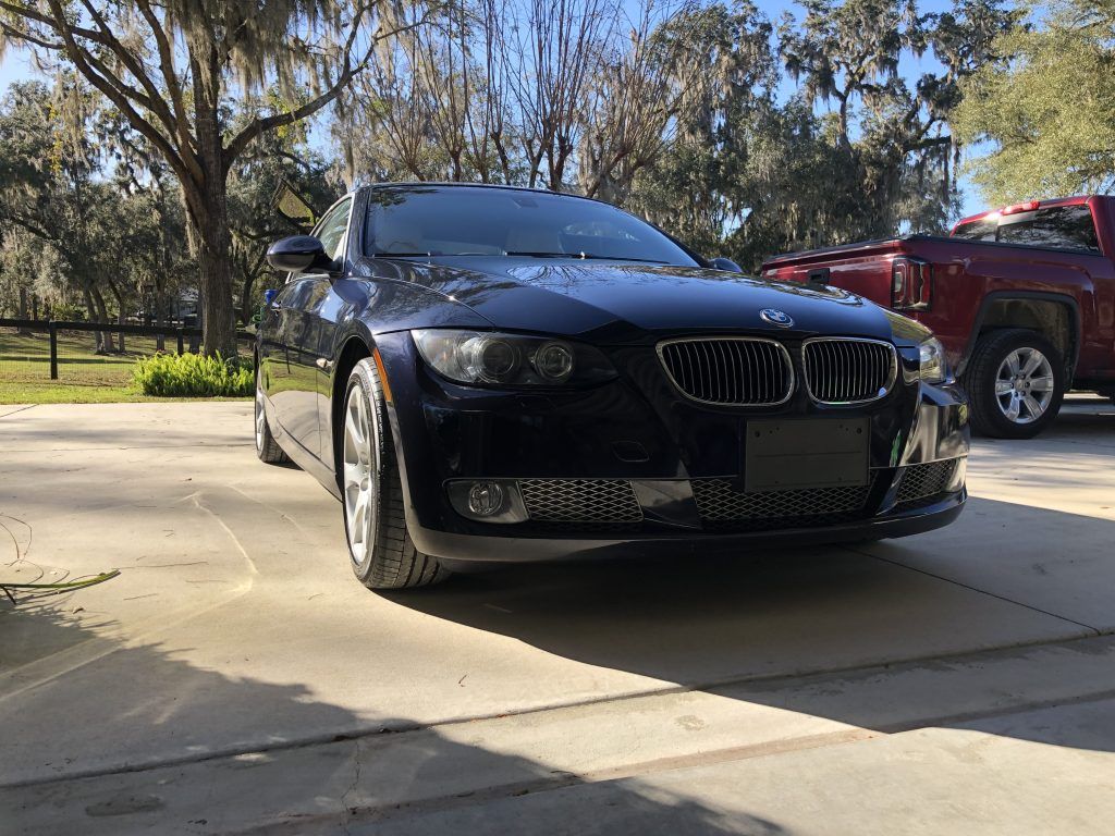 A black bmw is parked in a driveway next to a red truck.