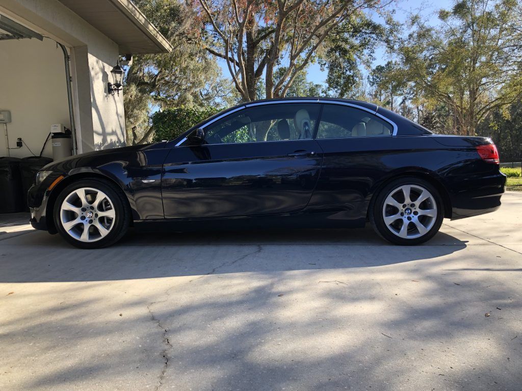 A black bmw 3 series convertible is parked in a driveway.