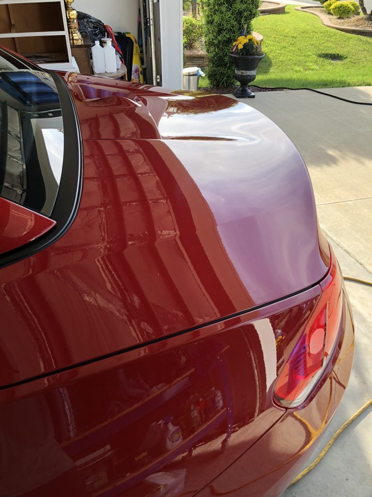 A red car is parked in a driveway in front of a garage.