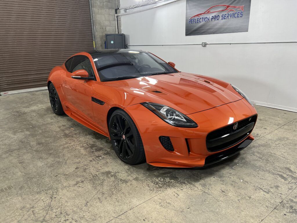 An orange jaguar f type is parked in a garage.