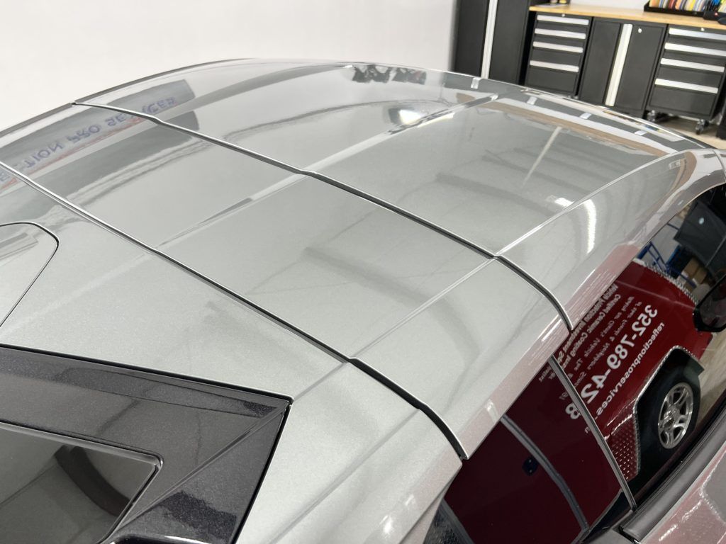 A silver car is parked in a garage with the roof visible